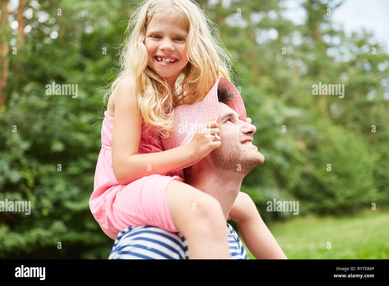 Laughing girl sits piggyback with father on the shoulders in the garden Stock Photo