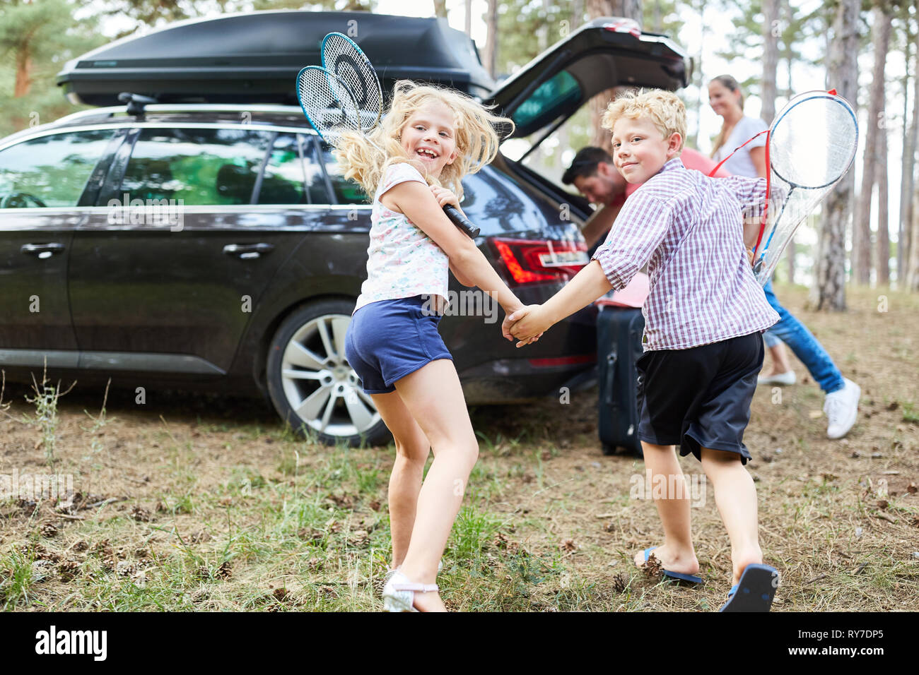 Sibling children are looking forward to the summer holidays and run to the car Stock Photo