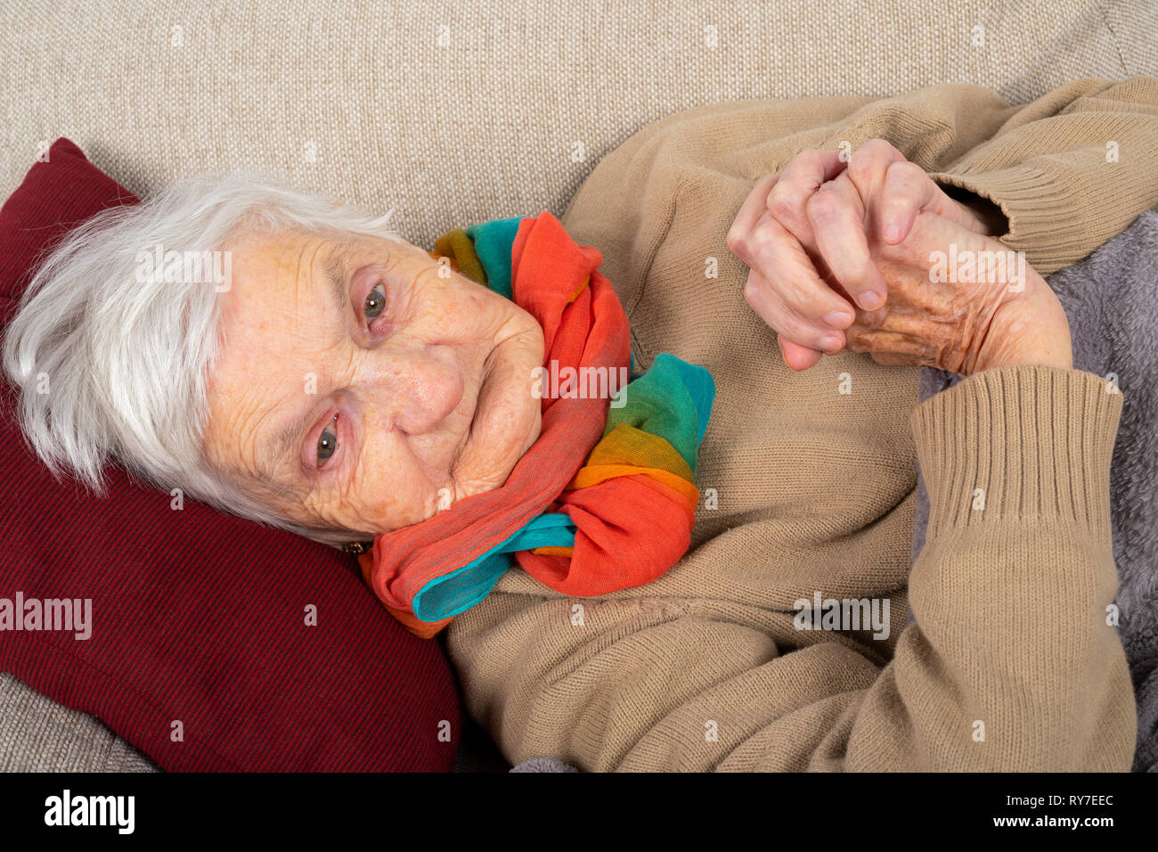 Close up picture of a sick old lady lying on the couch wrapped in a