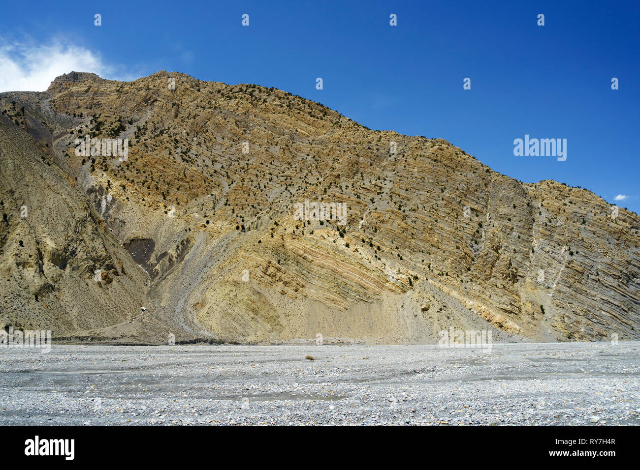 Rocky hill with visible geological stratas overhanging the dry riverbed of the Kali Gandaki between Jomsom and Kagbeni, Upper Mustang region, Nepal. Stock Photo