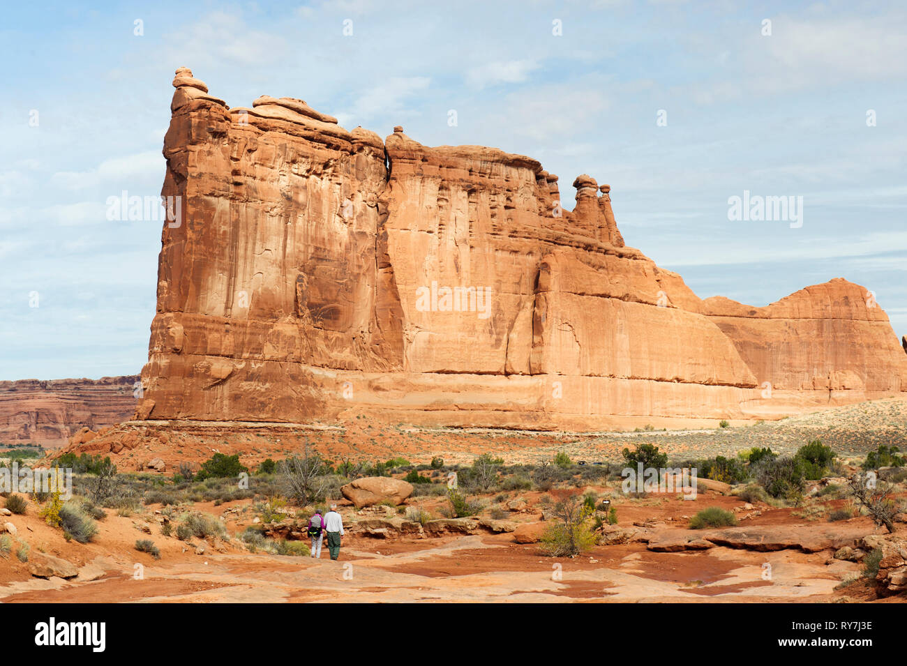 Two hikers approaching a gigantic sandstone formation known as the Tower of Babel on Park Avenue trail in Arches National Park, Utah, USA. Stock Photo