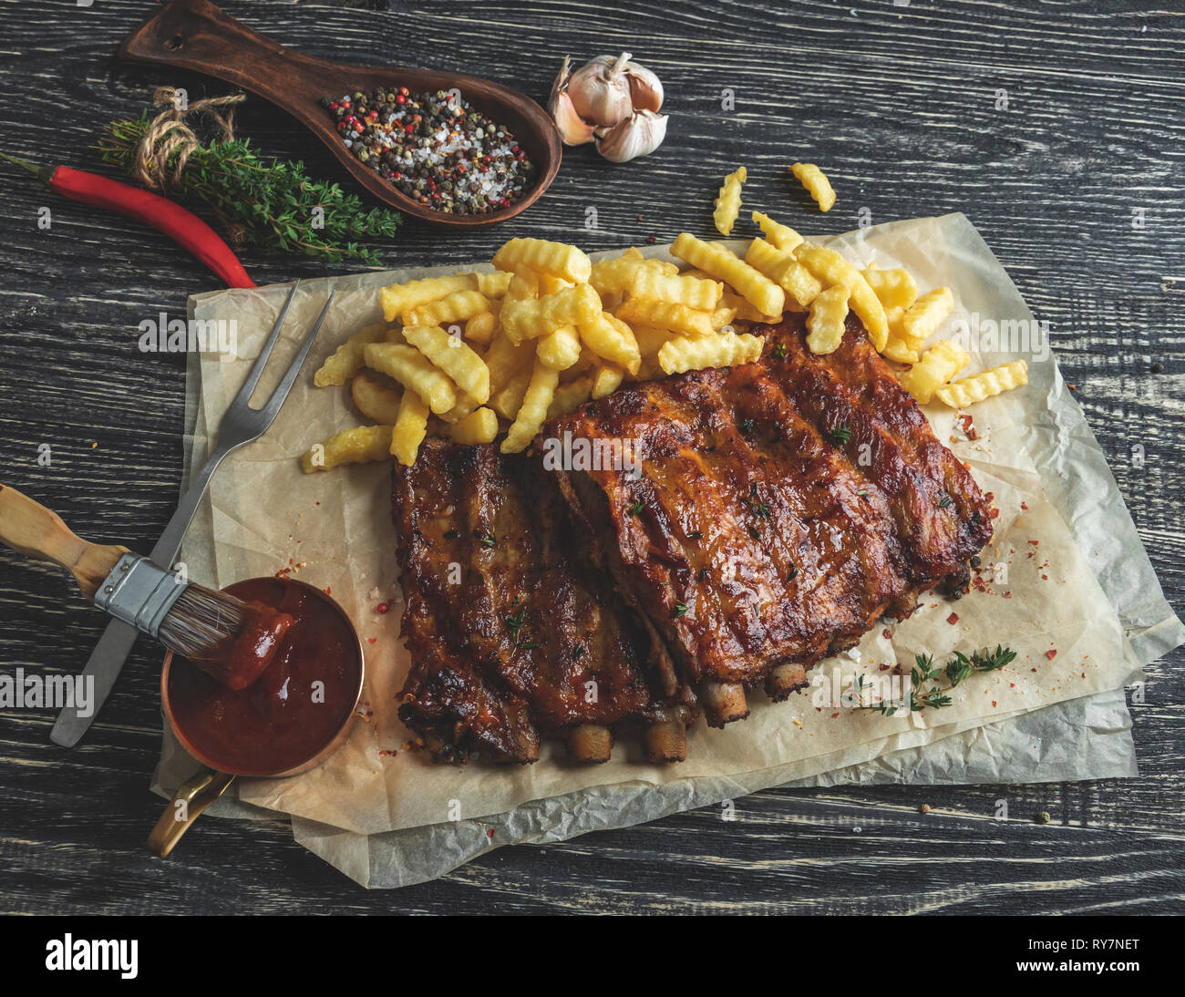 grilled pork ribs with sauce on a cutting board, french fries, spices, wooden background Stock Photo