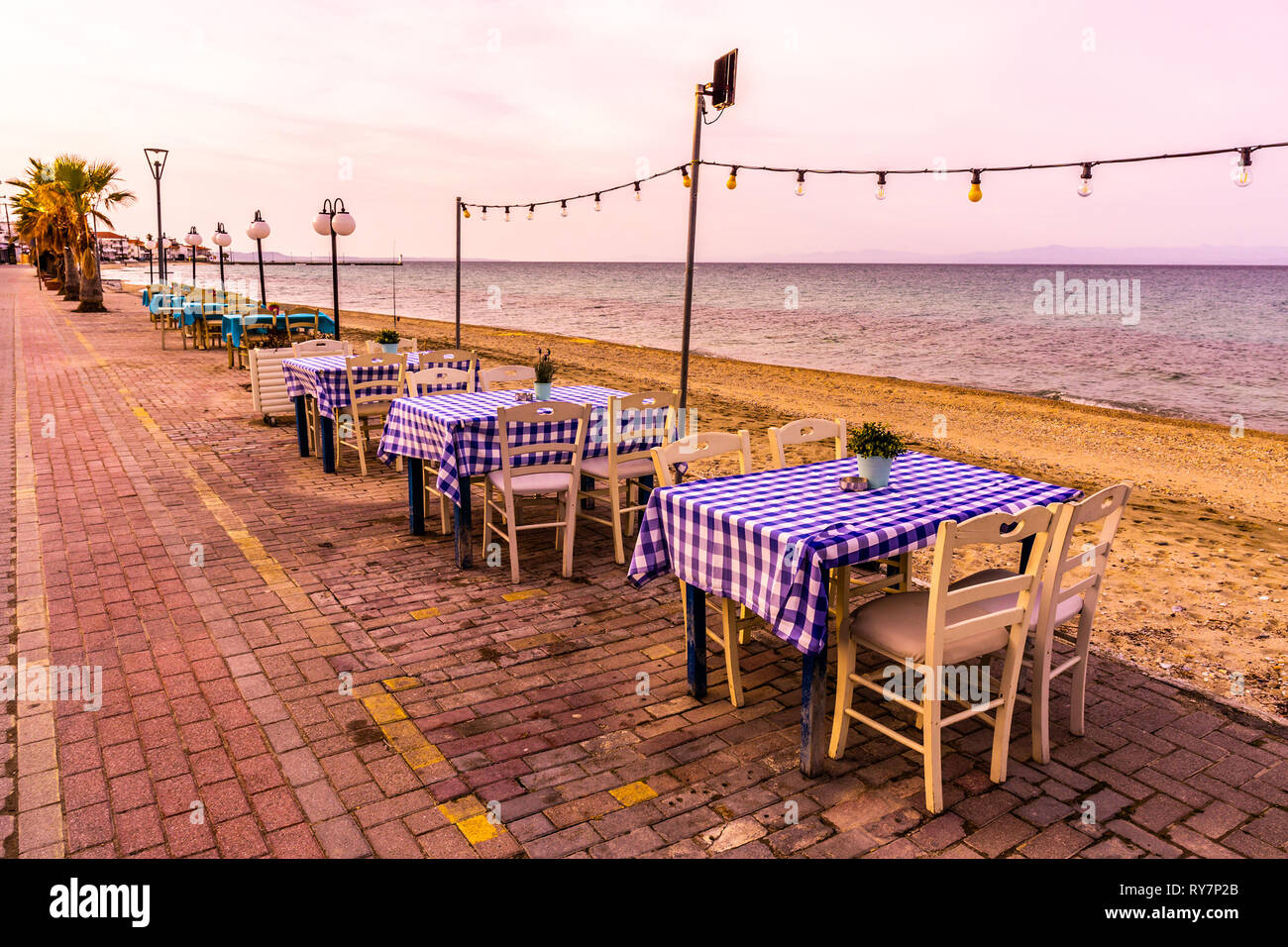 Pefkochori Promenade Street Empty Restaurant Tables and Chairs in a Row next to the Sandy Beach and Sea Stock Photo