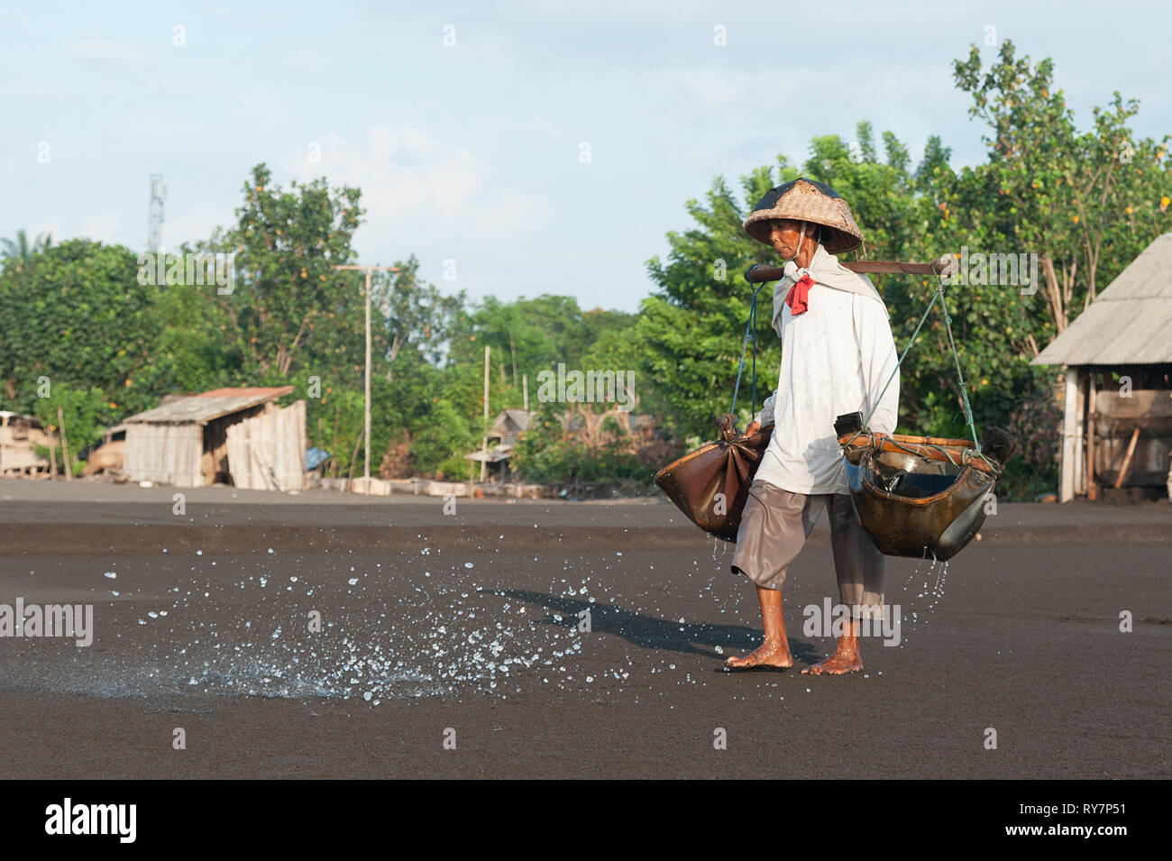 Bali Indonesia Apr 3, 2016 : Traditional salt farmer pouring sea water into black sand as a part of the process of producing traditional salt in Kusam Stock Photo