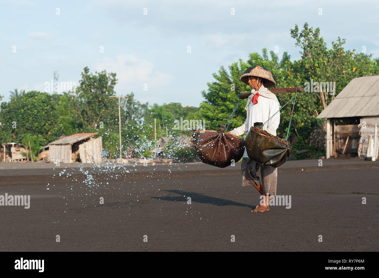 Bali Indonesia Apr 3, 2016 : Traditional salt farmer pouring sea water into black sand as a part of the process of producing traditional salt in Kusam Stock Photo