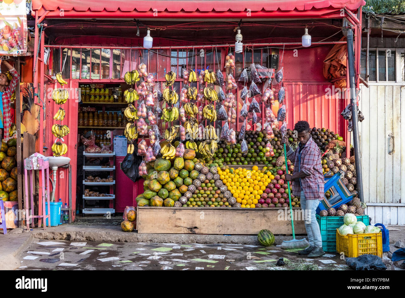ETHIOPIA, ADDIS ABABA, Man cleaning the pavement in front of his shop with a carefully arranged selection of tropical fruits, sweeping, Stock Photo