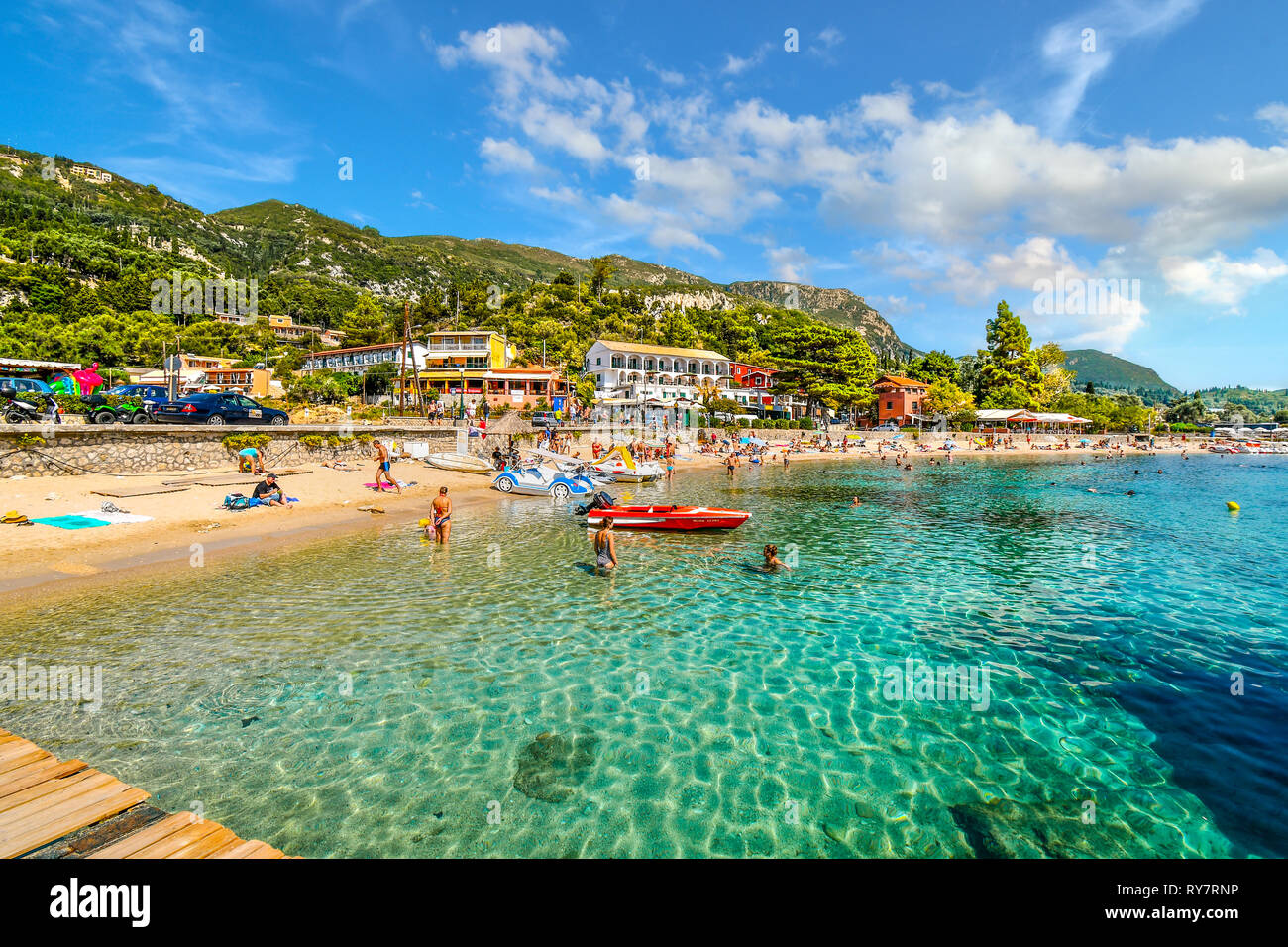 Tourists relax in the clear turquoise waters and on the sandy Palaiokastritsa beach on the Aegean island of Corfu, Greece. Stock Photo