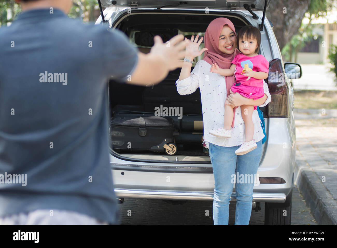 young muslim family , transport, leisure, road trip and people concept - happy woman and little girl waving at father to say goodbye and welcome besid Stock Photo