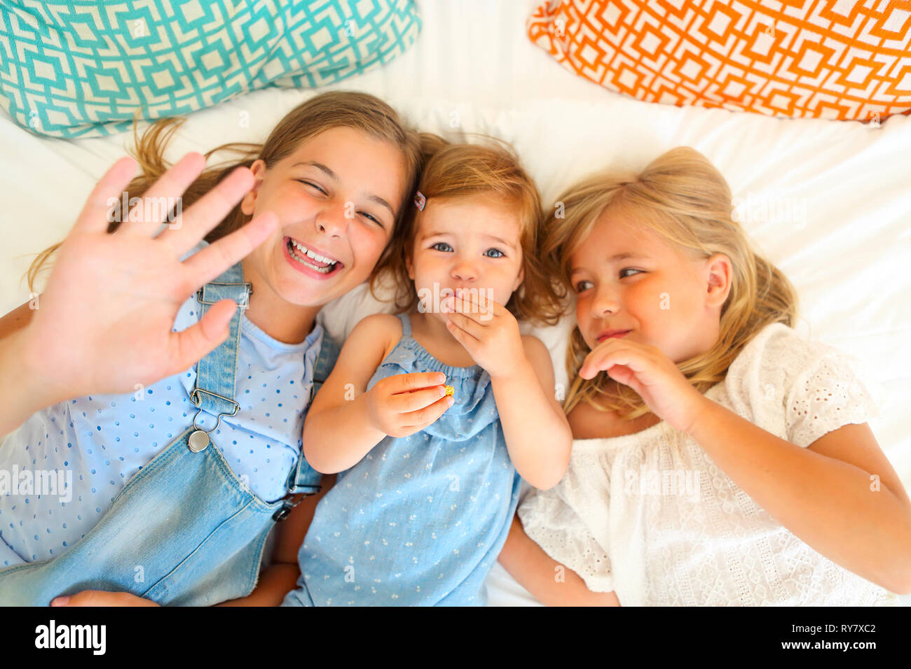 Portrait of the three happy little sisters on a bed having fun Stock Photo