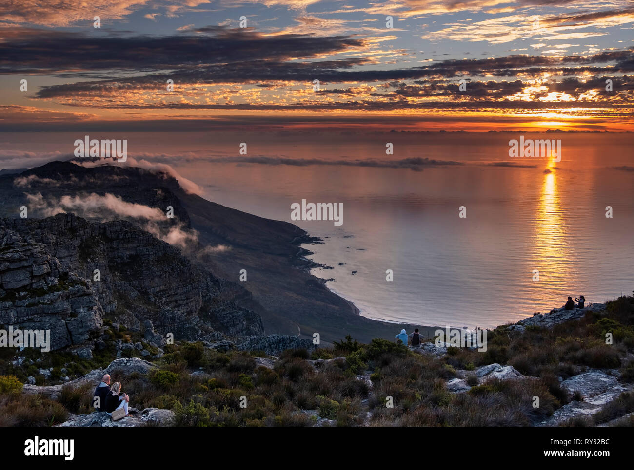 Couples watch sunset over the Twelve Apostles and Atlantic Ocean from Table Mountain, Cape Town, Western Cape, South Africa Stock Photo