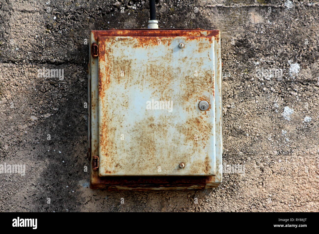 Partially rusted dilapidated locked metal electrical box mounted on