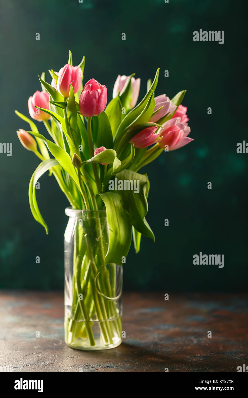 Bouquet of pink and lilac tulips in a glass vase on dark green ...