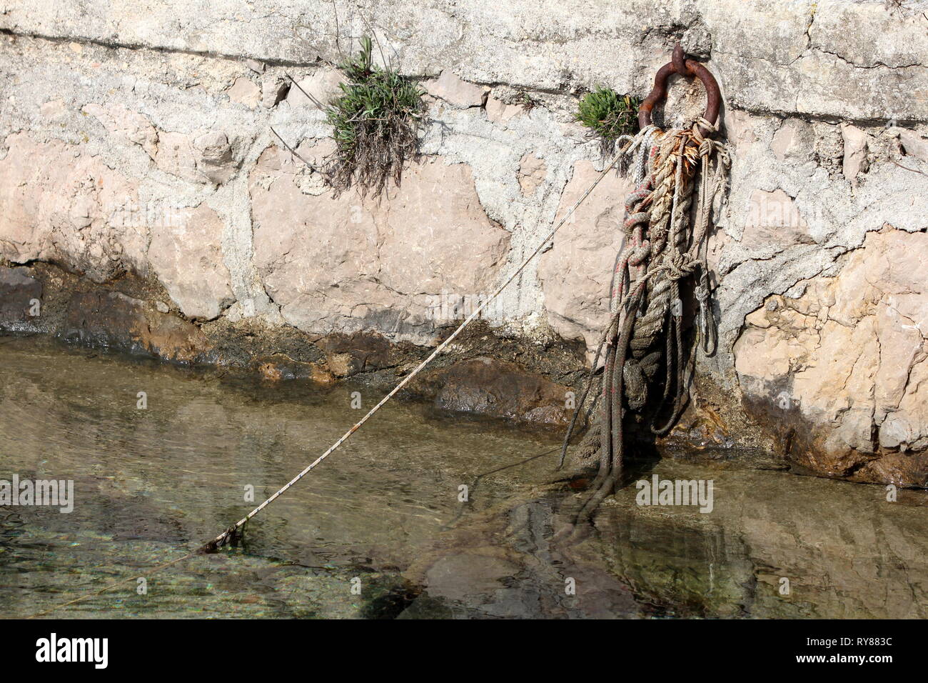 Strong naval ropes tied to rusted metal ring mounted on local stone