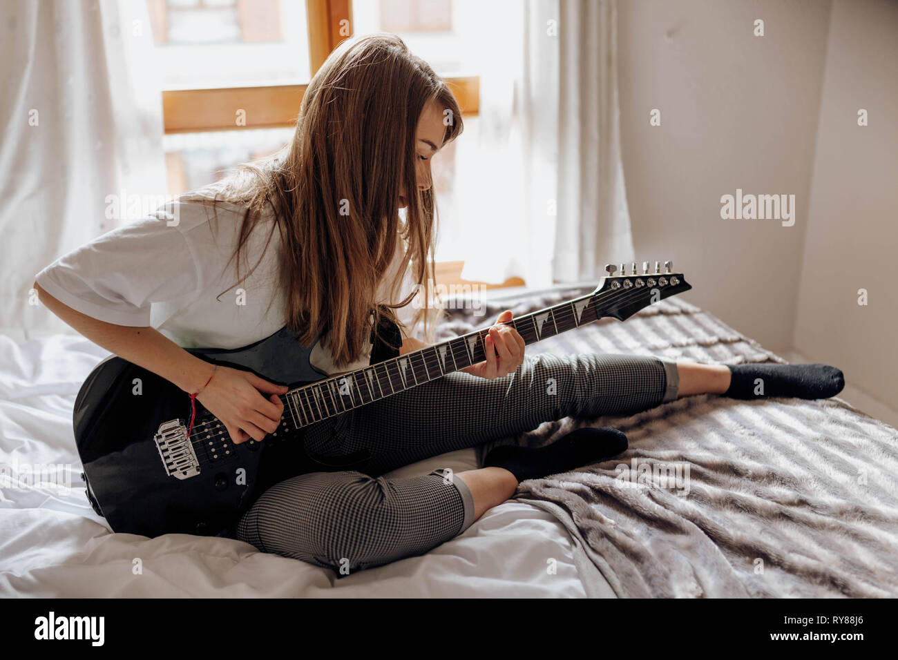 side view of Young brunette Woman playing guitar on bed Stock Photo - Alamy