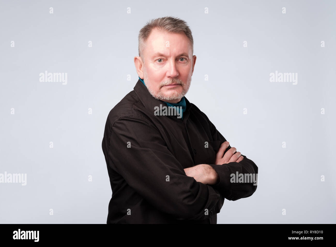 old man in black shirt with folded hands looking at camera with confidence Stock Photo