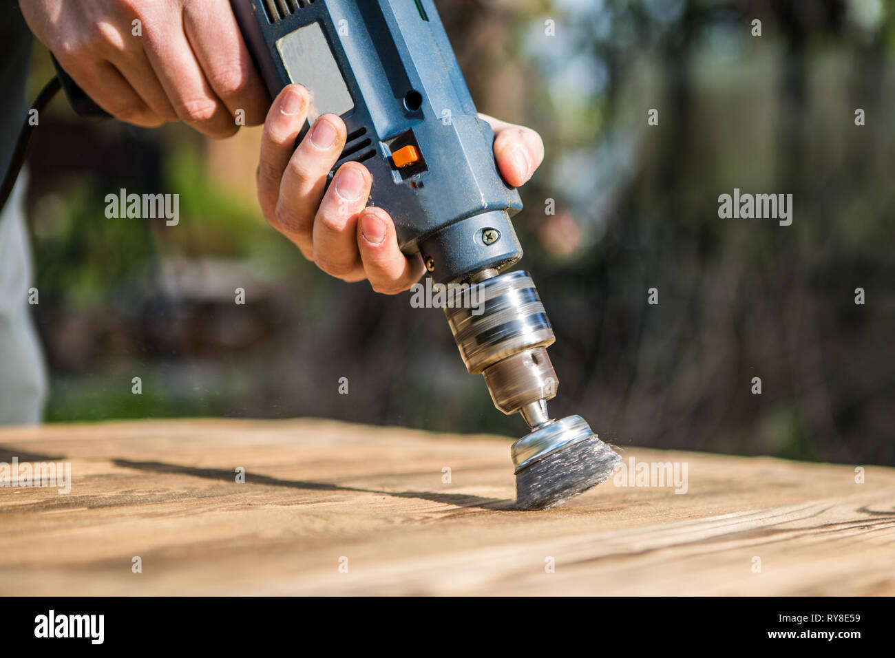 Hands man with electrical rotating brush metal disk sanding a piece of ...
