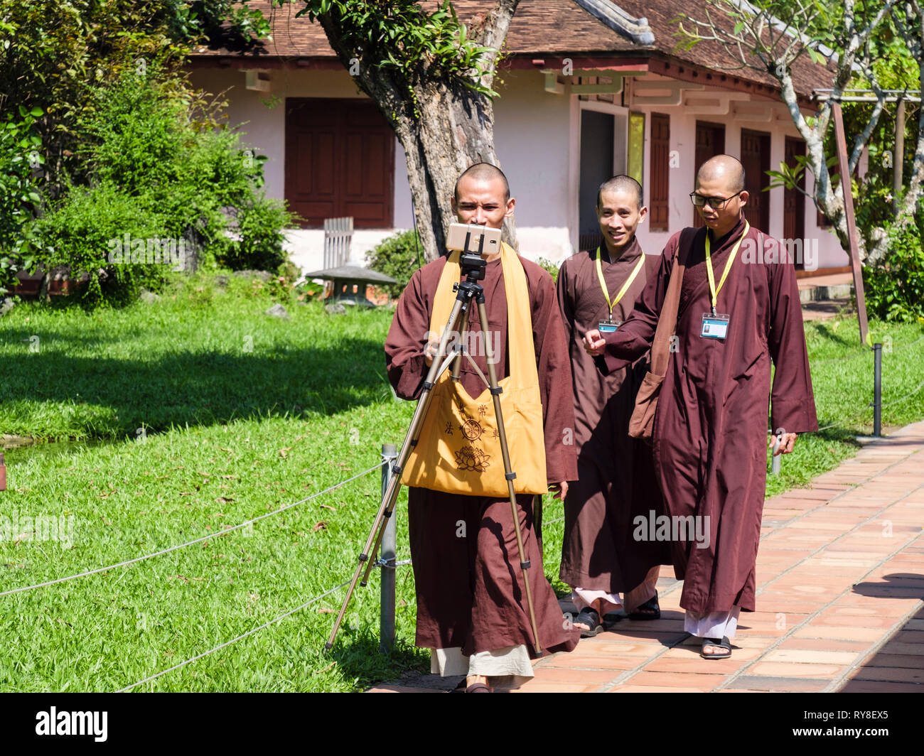 Monks walking and taking a selfie on a mobile phone at Thien Mu Pagoda complex. Hue, Thừa Thien–Hue Province, Vietnam, Asia Stock Photo