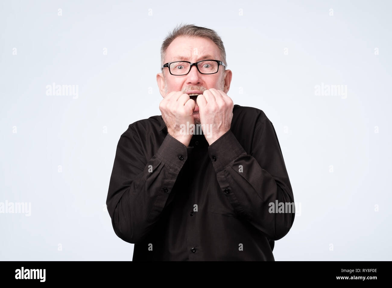 Nervous senior man in glasses bites nails, looks worried before visiting doctor Stock Photo