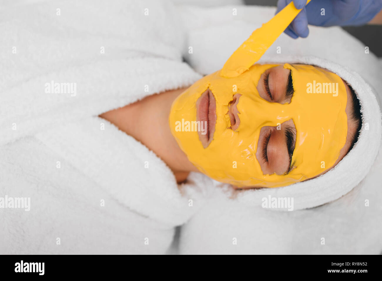 Beautician applying facial mask with orange extract on beautiful female face. Herbal Medicine Stock Photo