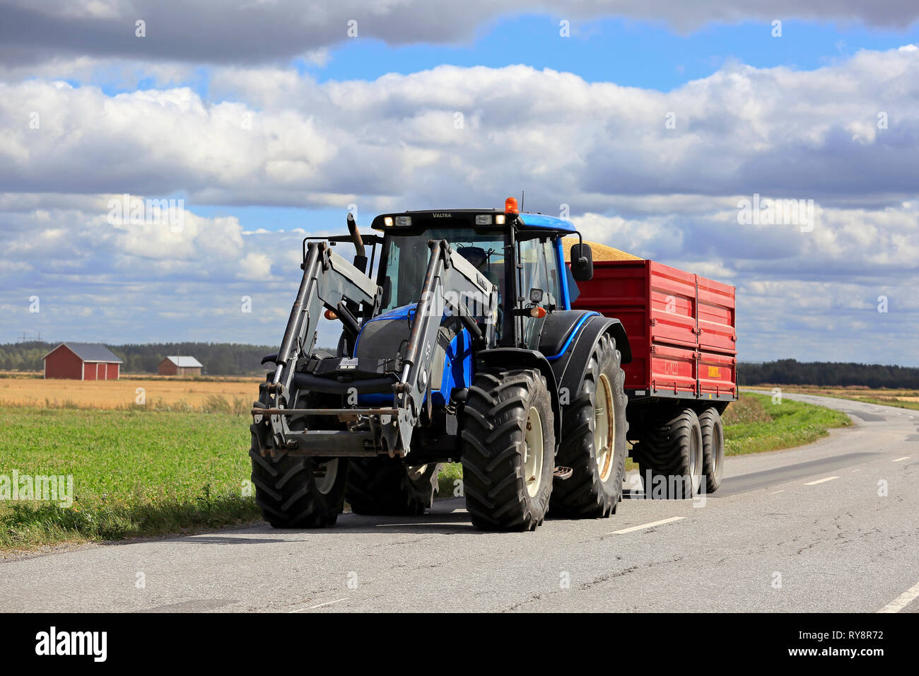 Ilmajoki, Finland - August 11, 2018: Blue Valtra farm tractor pulls trailer load of harvested grain along rural road on a clear day of autumn harvest. Stock Photo