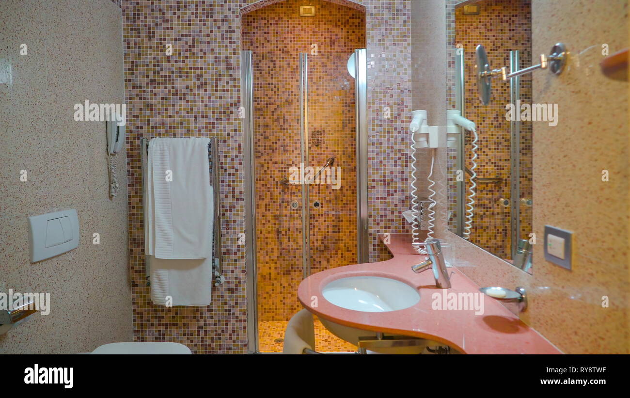 The look inside the bathroom of the hotel room with the marble tiles pink small sink and shower room Stock Photo