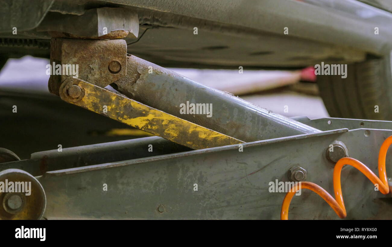 The rusty car jack underneath the car in the shop that is being
