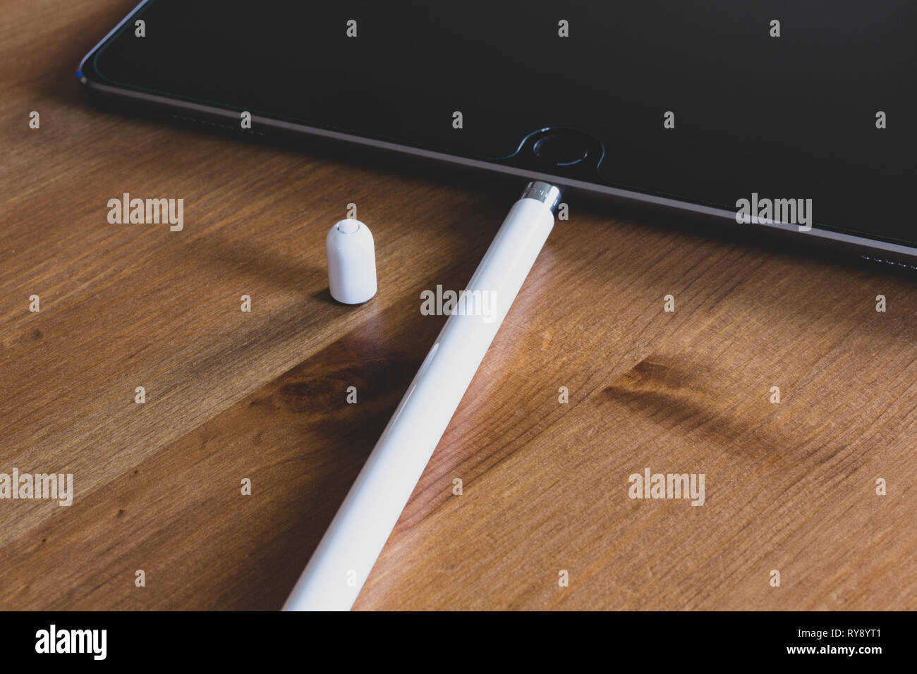 Apple Pencil 2015 1st generation connected to iPad Pro charging on natural wooden table Stock Photo