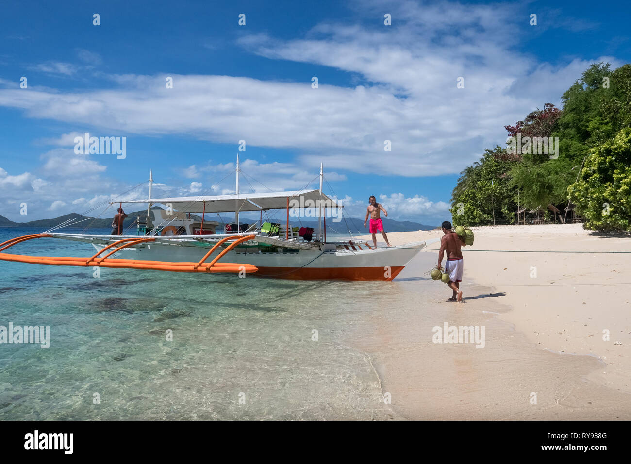Filipino tour guide brings coconuts to Dutch tourist in boat Linapacan Island beach, Palawan