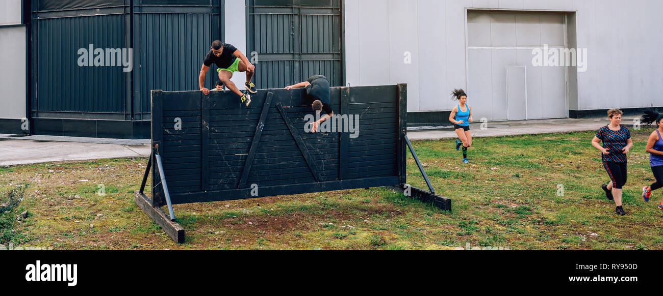 Participants in obstacle course running and climbing wall Stock Photo
