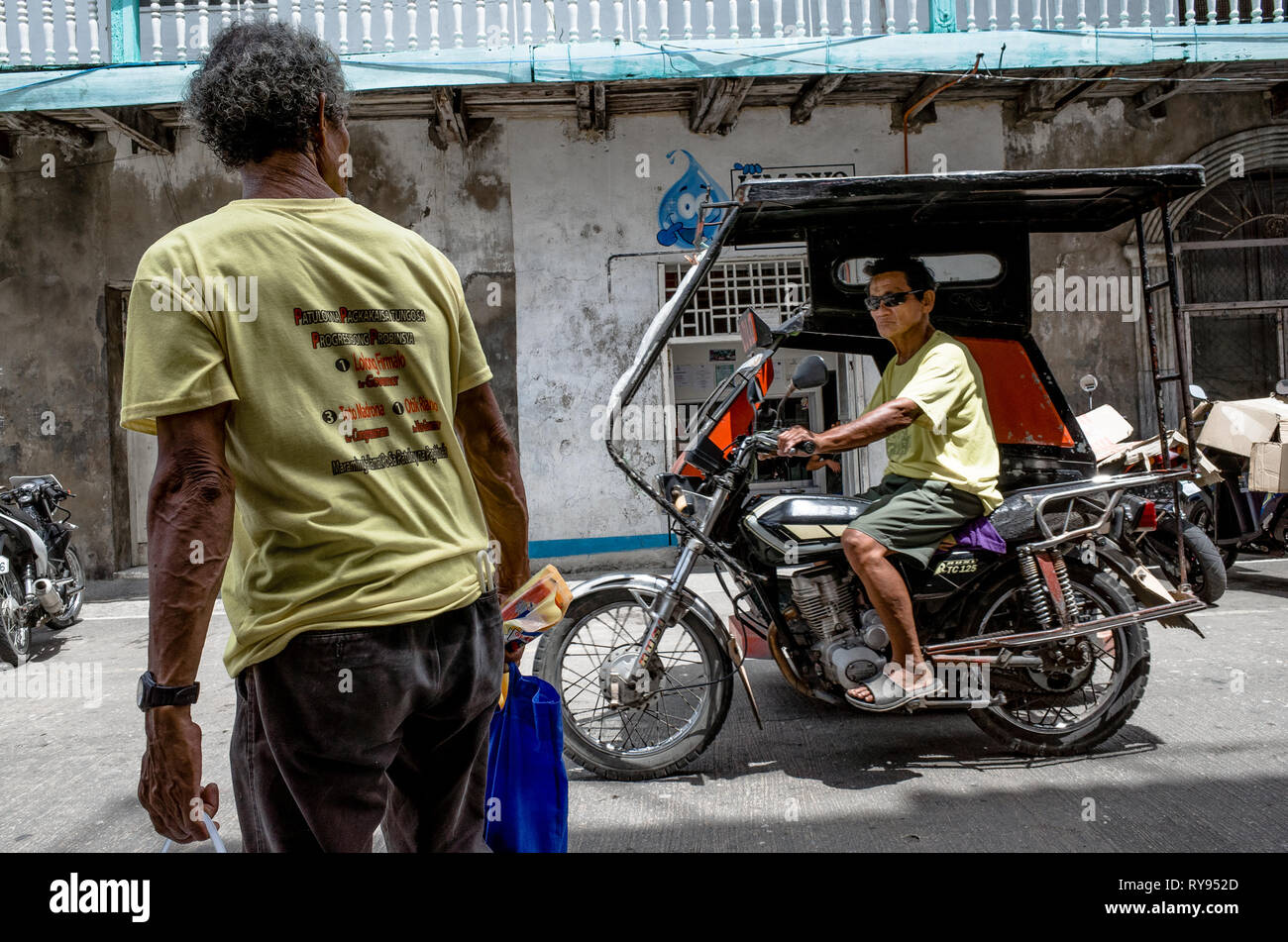 An elderly Filipino man watches a tricycle driver pass by on the street - Romblon City, Philippines Stock Photo