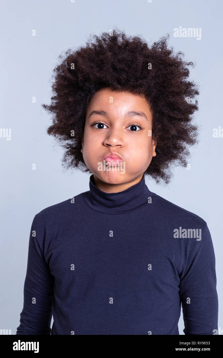 African American dark-haired kid inflating cheeks while wearing blue turtleneck Stock Photo