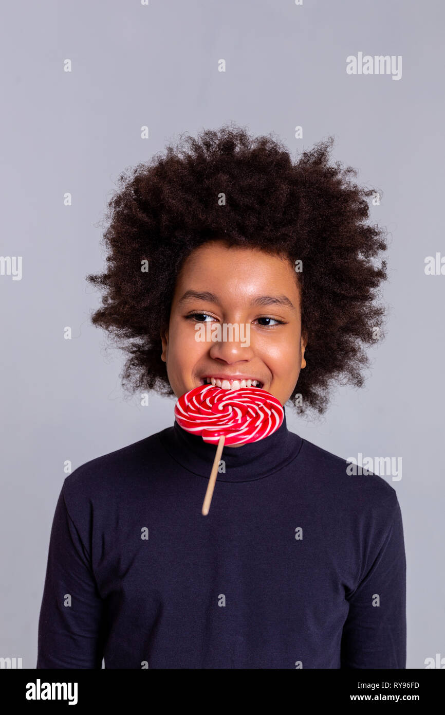 Funky darkhaired curly boy biting hard candy with strong teeth Stock
