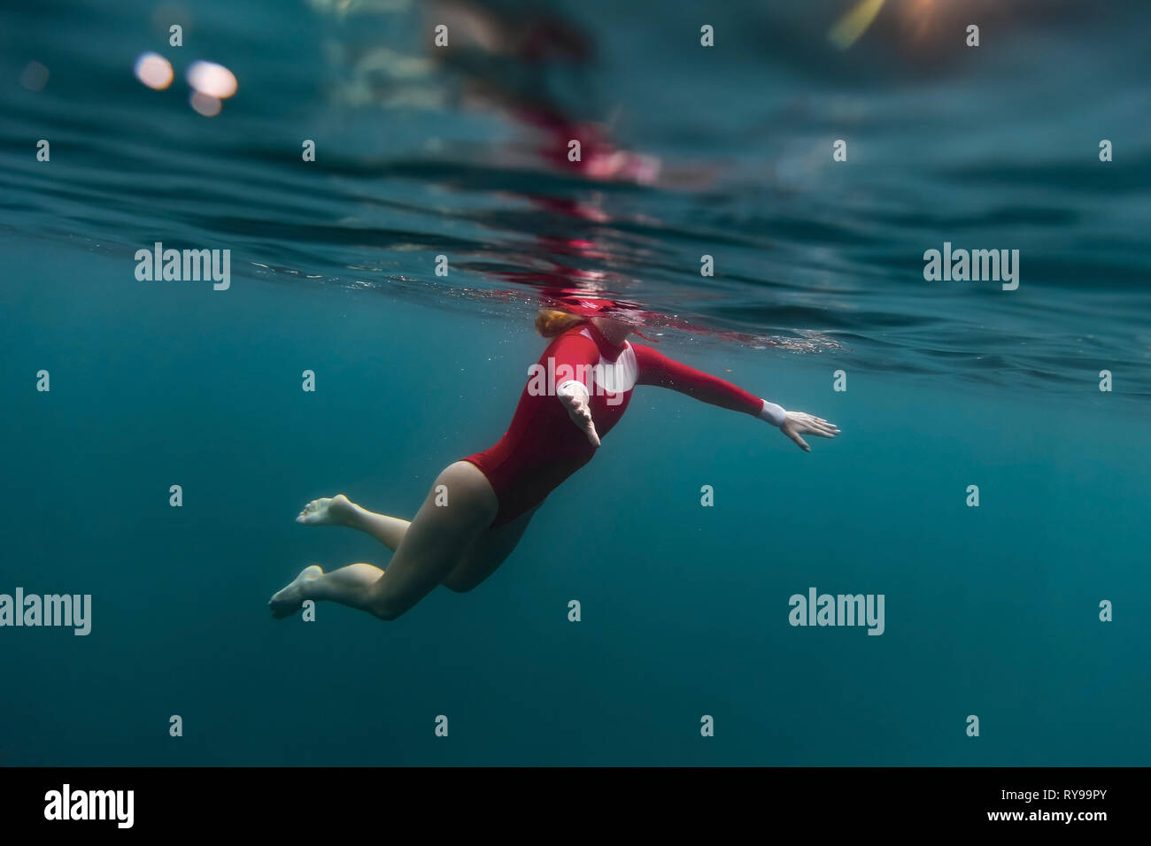 Side view of female in red swimsuit diving in blue water of sea on Bali