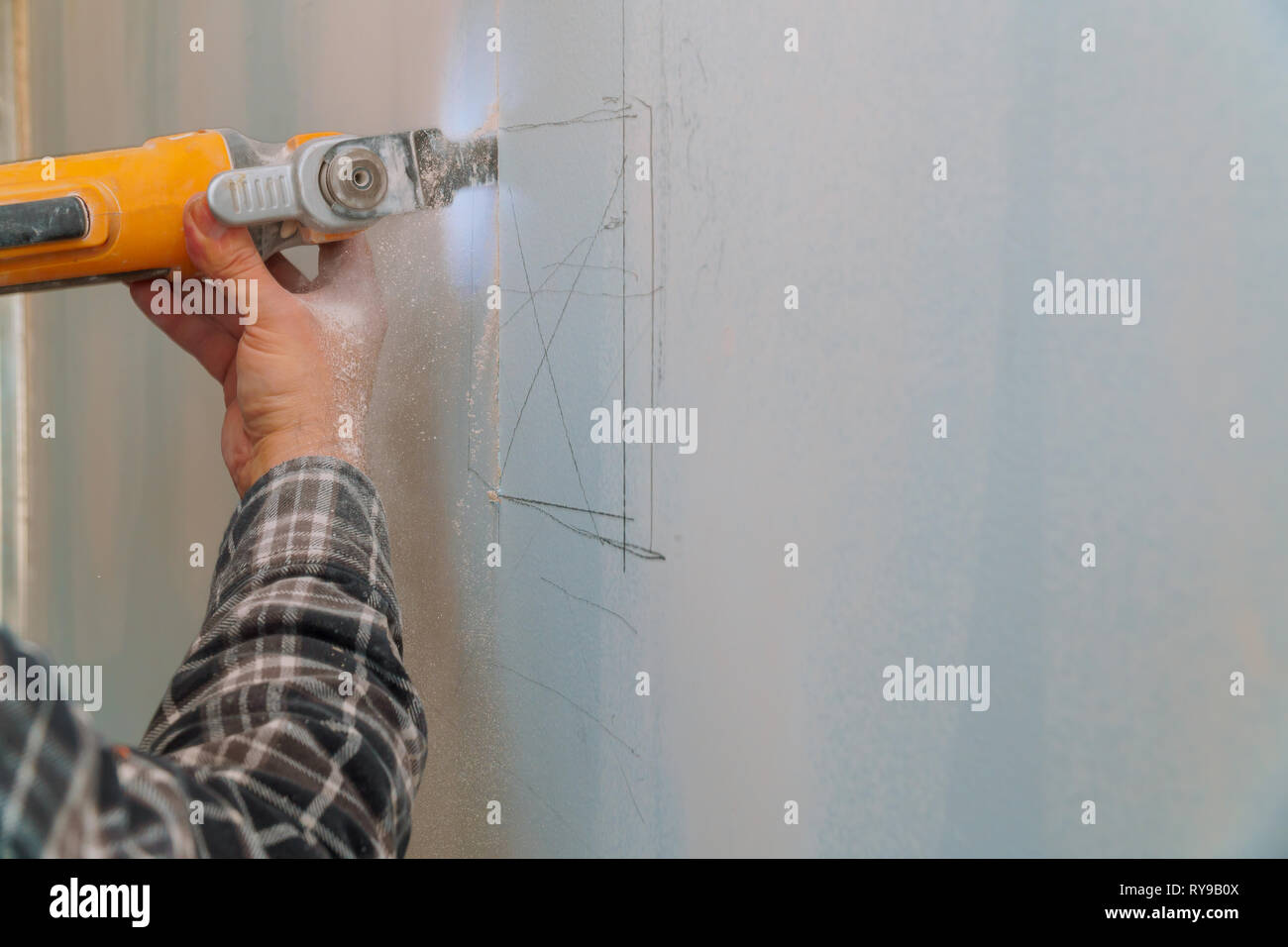 Construction worker cutting gypsum drywall by using electric cutter