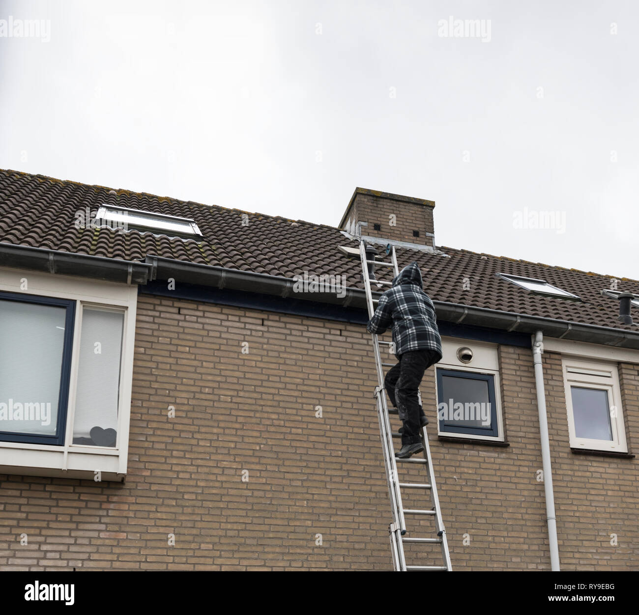 man climbing on a ladder doing inspection of the roof of a house Stock