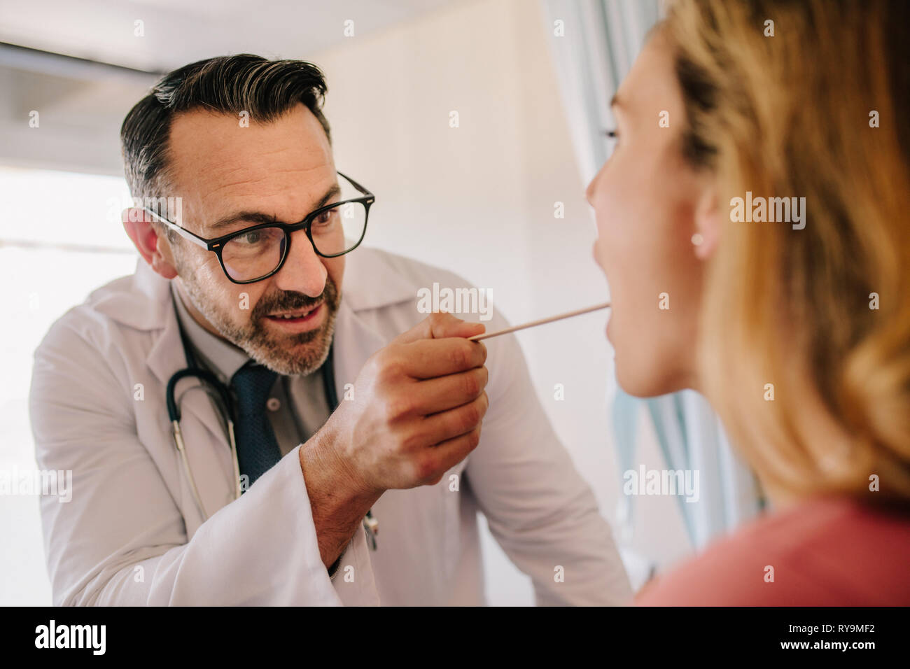 Male doctor checking throat of a female patient with the medical stick