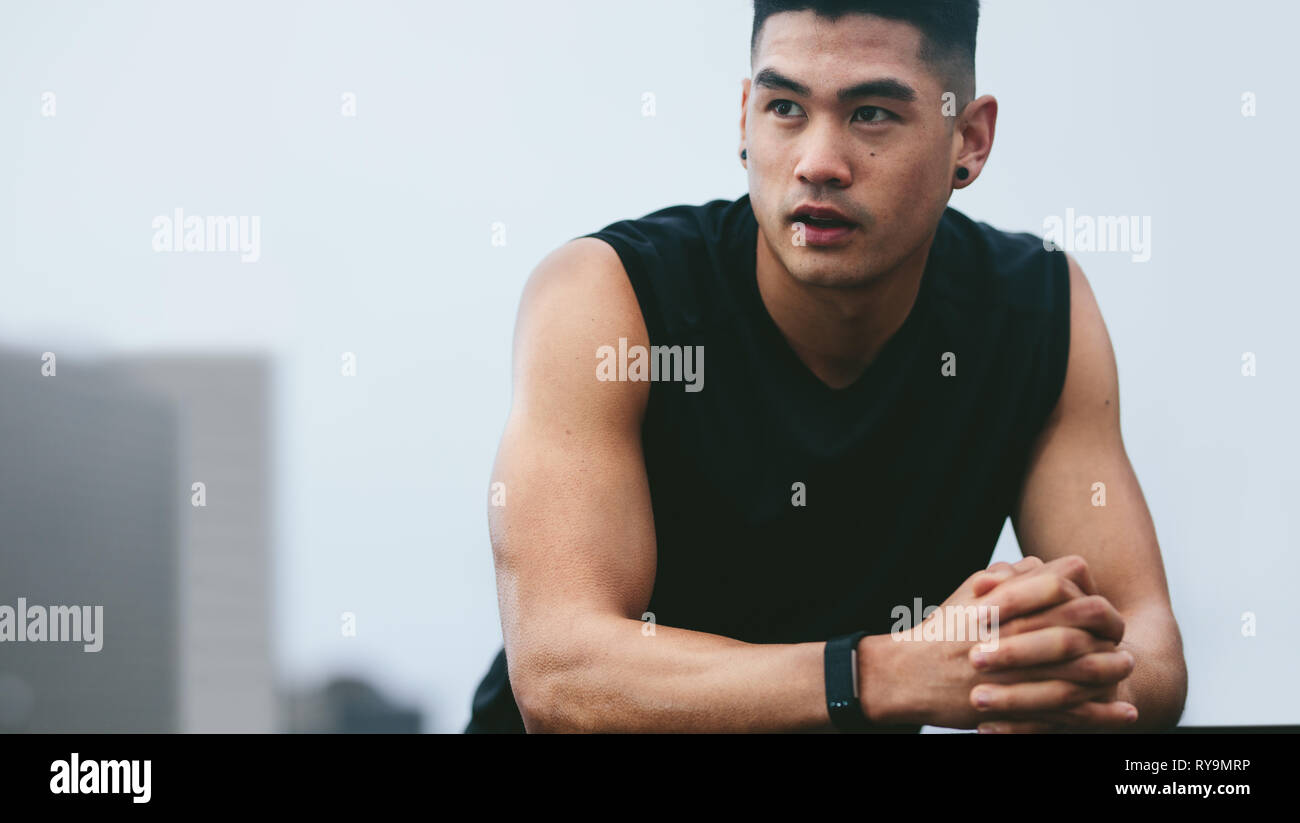 Muscular asian man standing outside and looking away. fitness male model in sports clothing resting after his workout. Stock Photo