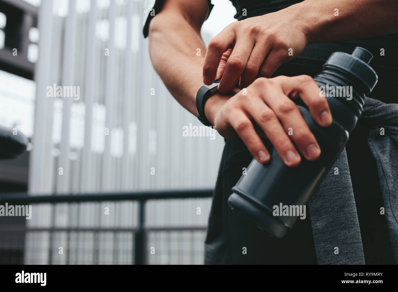 Close up of man with water bottle checking his performance on fitness app on his smart watch. Male using a smartwatch to monitor his progress . Stock Photo
