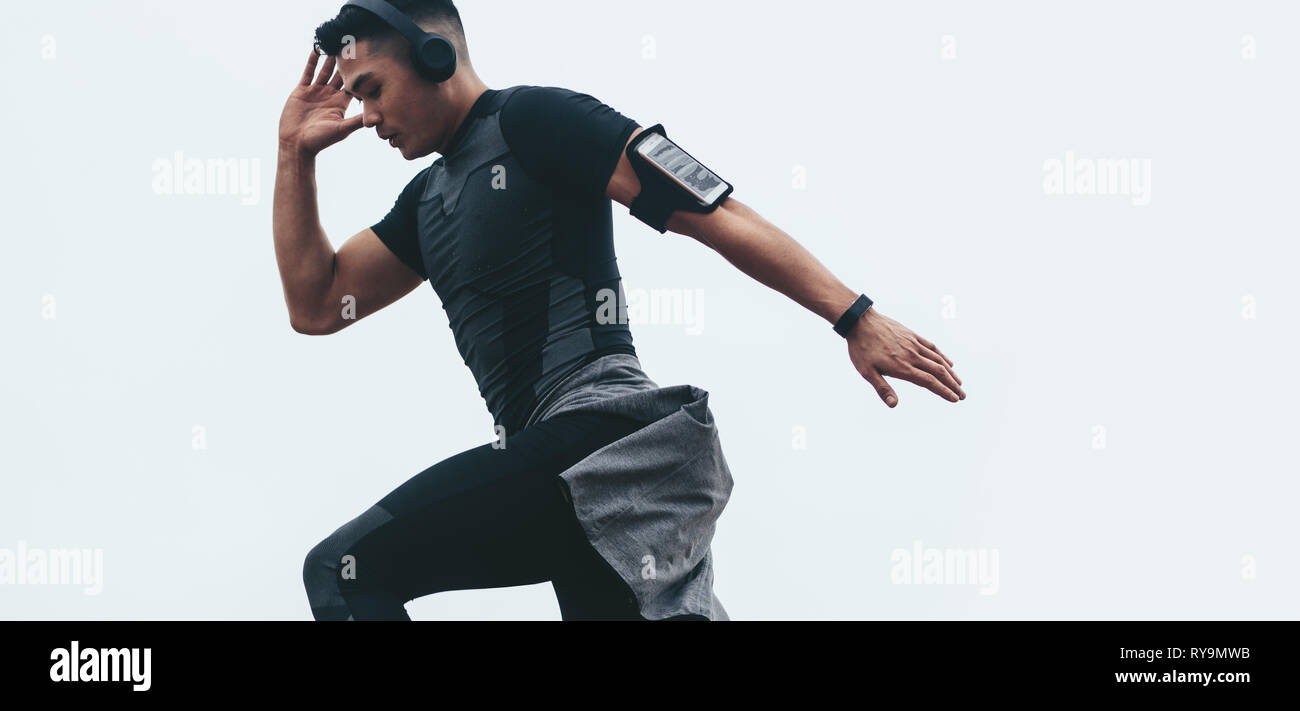 Fit asian man doing workout. Young asian man in black sports clothing stretching with headphones on and mobile on arm band. Stock Photo