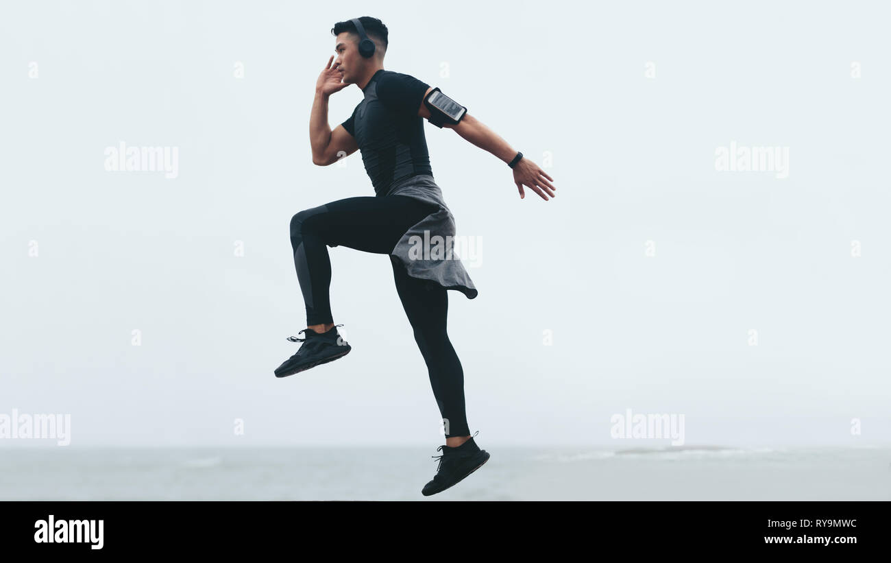 Sporty asian man doing intense exercises. Side view of fitness male exercising jump and lunge. Stock Photo
