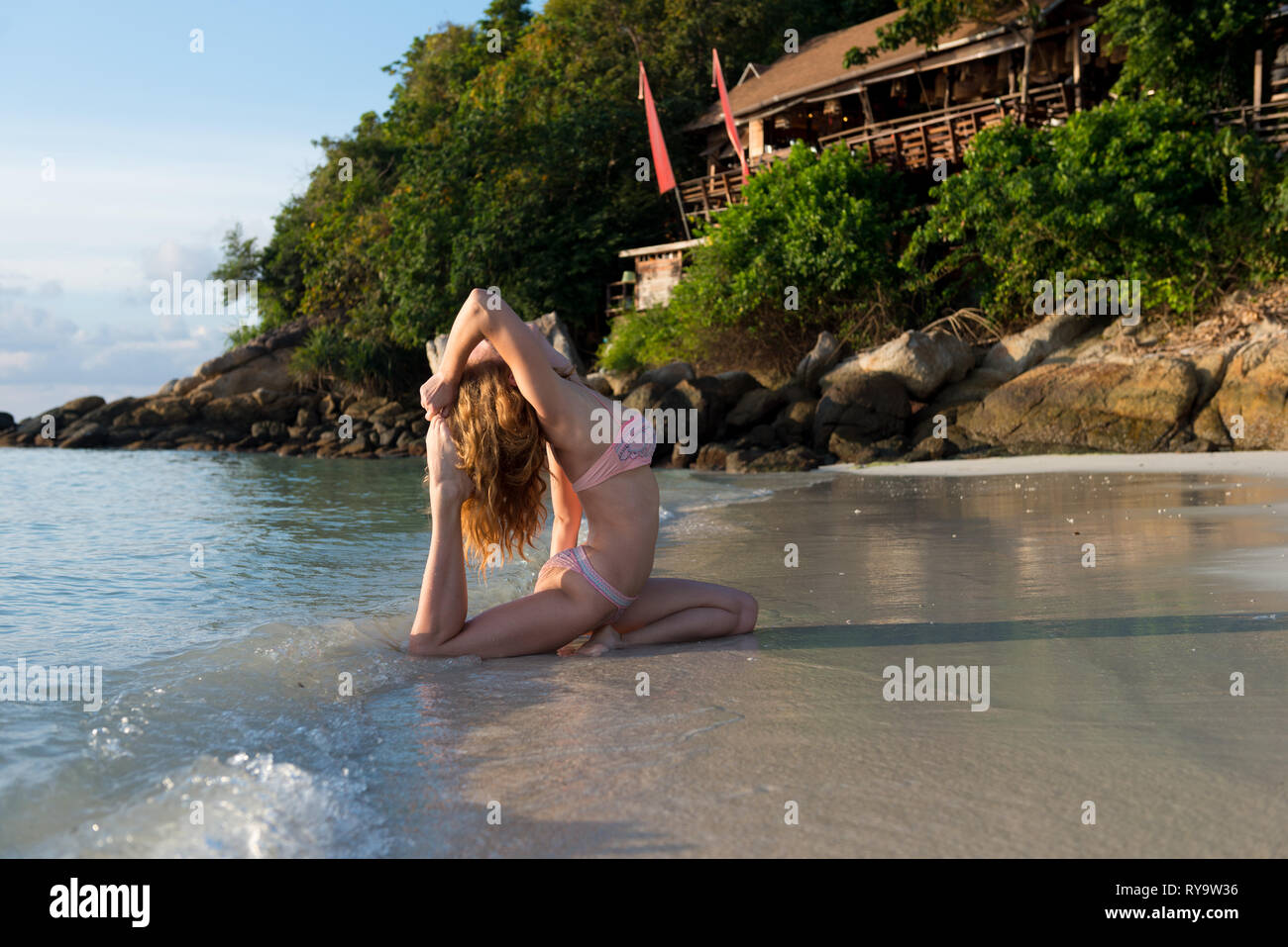 Girl practicing yoga pigeon pose in rolling waves. Ko Lipe island, Thailand Stock Photo