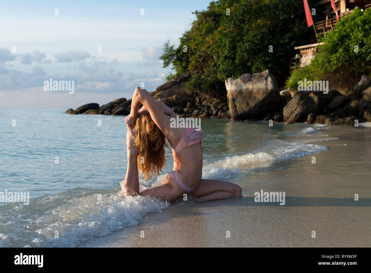 Yoga in the waves of Andaman sea - girl in pigeon pose practicing yoga at sunrise. Koh Lipe, Thailand Stock Photo