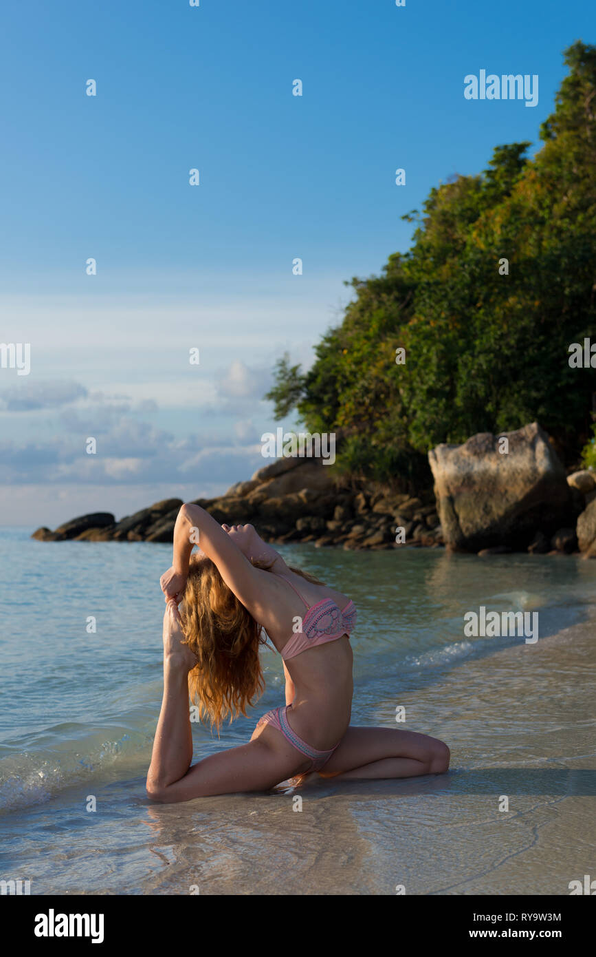 Yoga on the beach in Thailand - girl in pigeon pose on Sunrise beach, Ko Lipe island Stock Photo