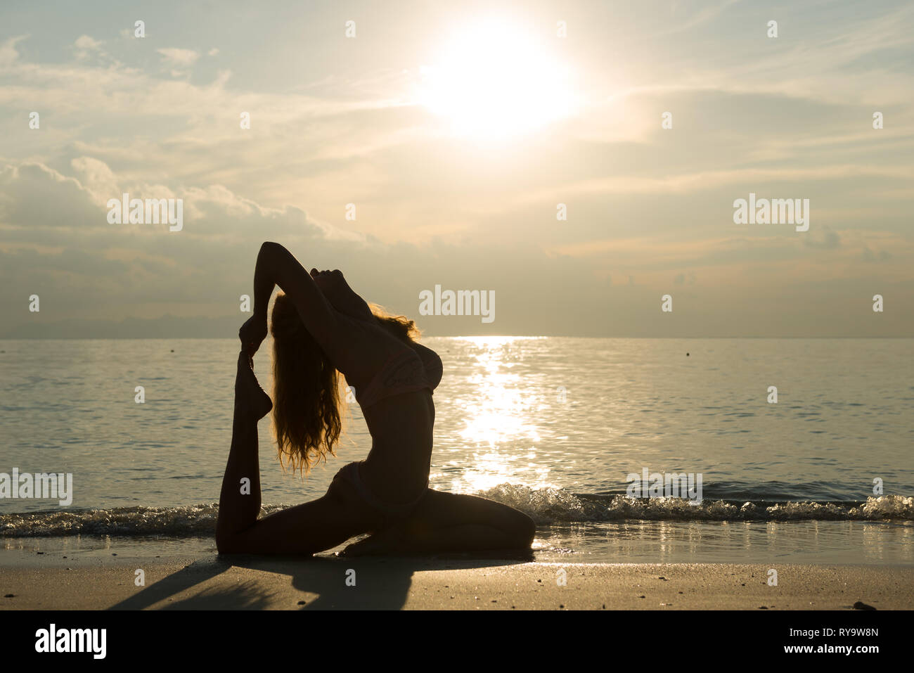 Silhouette of a girl in pigeon pose, practicing yoga on the beach, Thailand Stock Photo