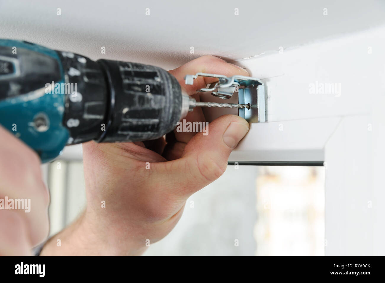 Installing wooden blinds. A man drill hole for fastening metal bracket