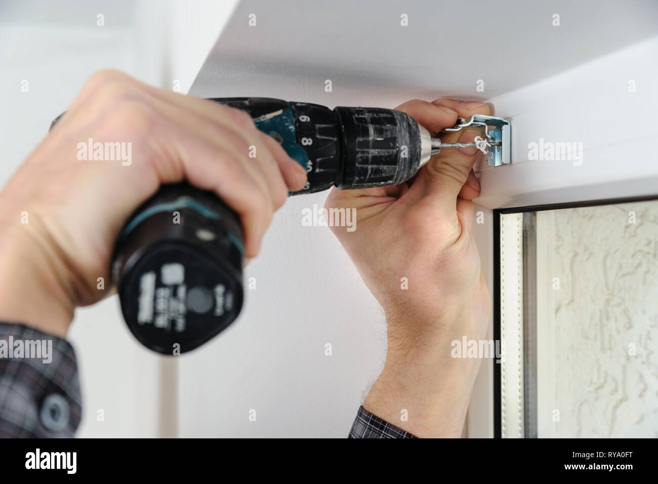 Installing wooden blinds. A man drill hole for fastening metal bracket