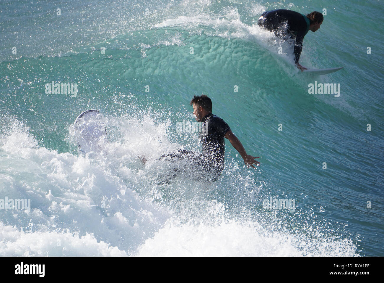Two surfers riding the crest of a wave on an azure ocean Stock Photo ...