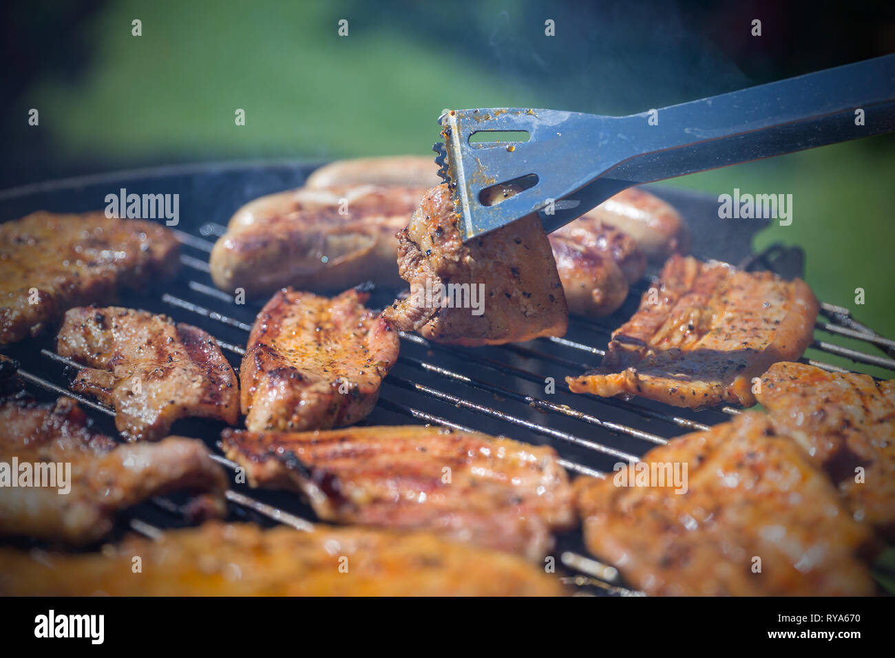 Bauchfleisch und Wuerstchen auf dem Grill, ein Stueck Bauchfleisch wird mit einer Grillzange umgedreht bei THEMENBILD Grillen, 06.05.2018 Foto: Mario  Stock Photo