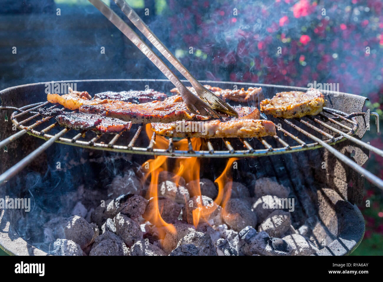 Bauchfleisch und Wuerstchen auf dem Grill, unter dem Grill lodern die Flammen, ein Fleischstueck wird umgedreht bei THEMENBILD Grillen, 06.05.2018 Fot Stock Photo