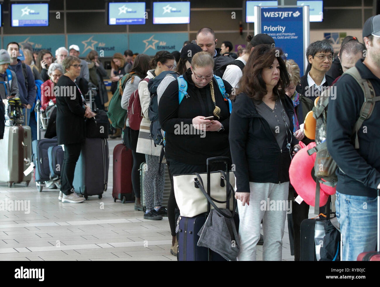 Vancouver, Canada. 13th Mar, 2019. Passengers line up at the departure hall at Vancouver International Airport in Richmond, Vancouver, Canada, March 13, 2019. Canada is grounding all its Boeing 737 Max 8 and 9 aircraft and banning the jets from its airspace following the Ethiopian Airlines crash that killed all 157 people on board, including 18 Canadians. Credit: Liang Sen/Xinhua/Alamy Live News Stock Photo